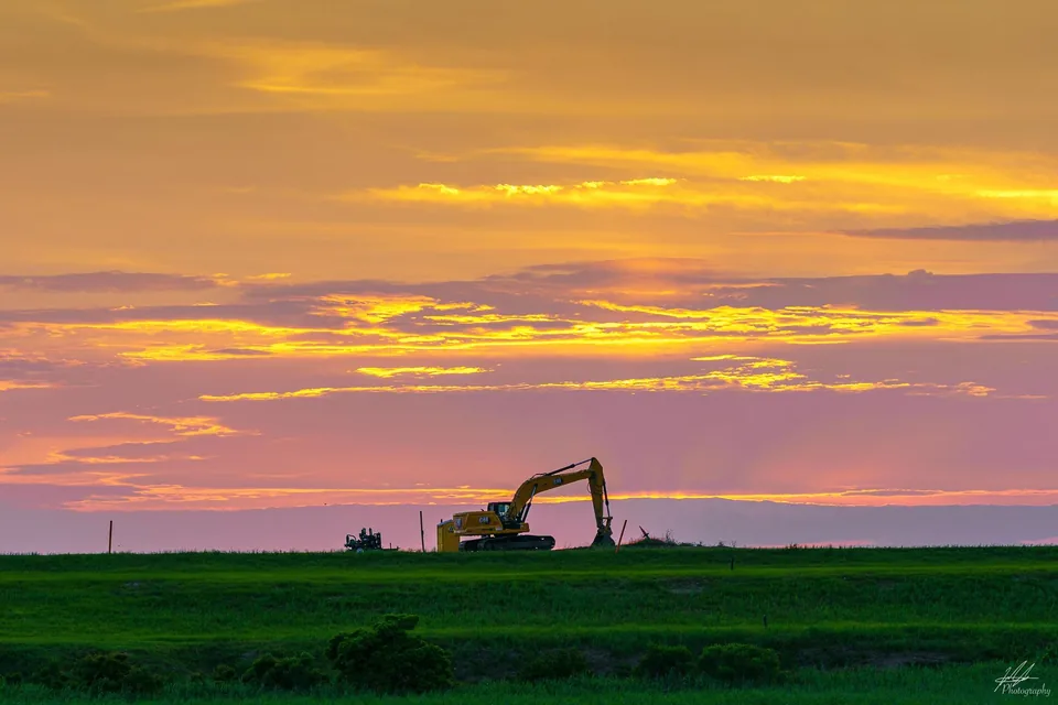 Excavator silhouetted against a golden sunset sky