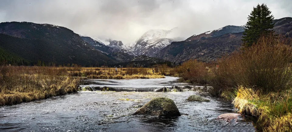 Mountain creek winding through a meadow under clouds
