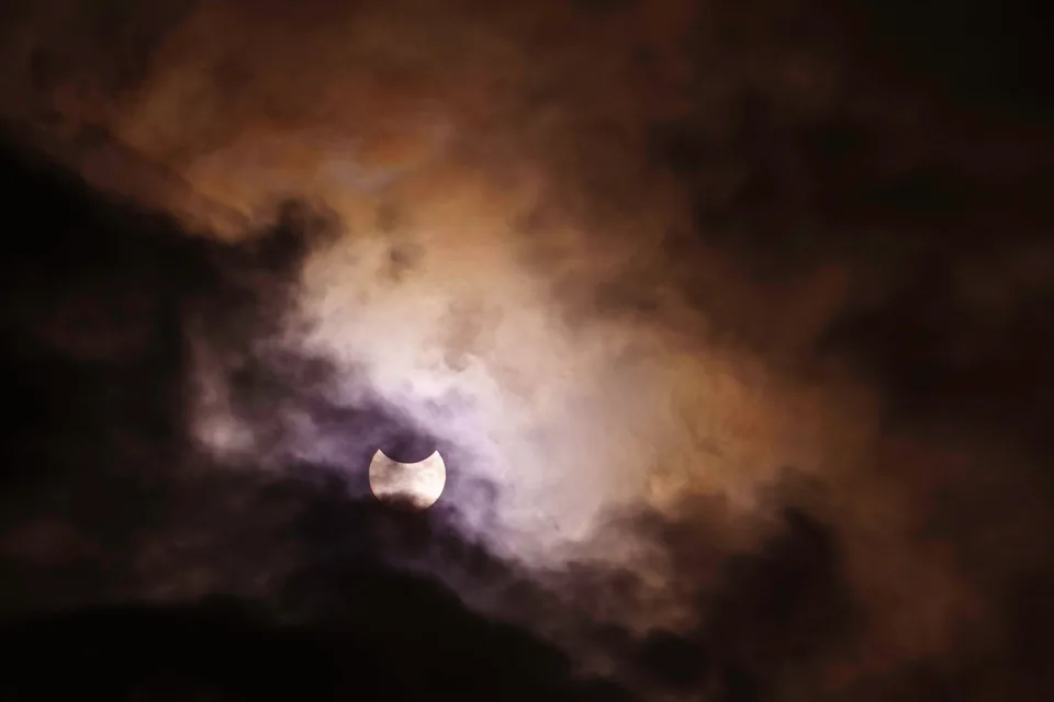 Partially eclipsed sun peeking through clouds