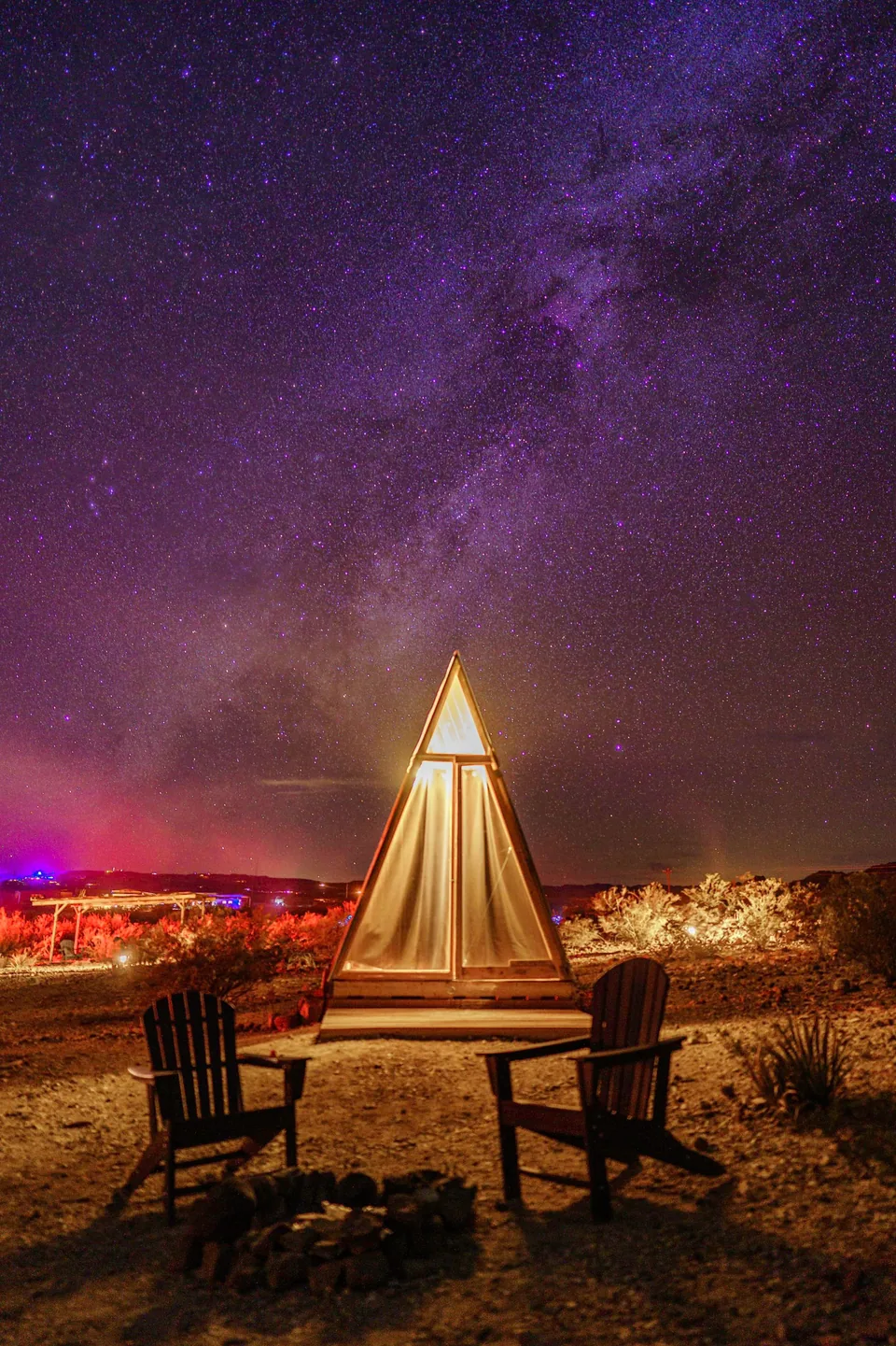 Glowing A-frame tent and chairs under the Milky Way