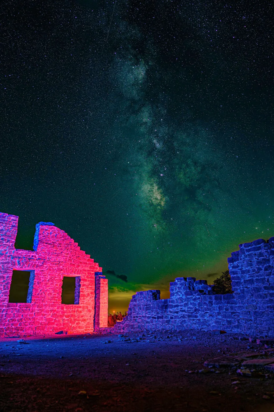 Ruins lit pink and blue under the Milky Way
